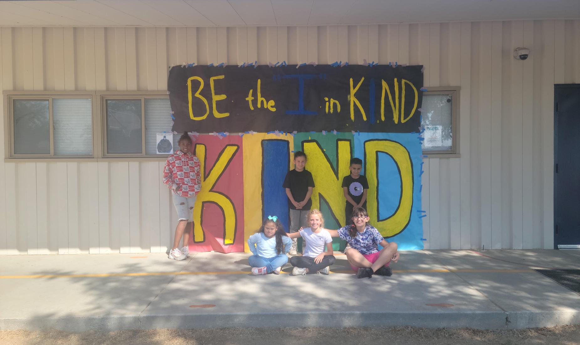 Students posing next to large"Be the I in Kind" poster for Anti-Bullying Month