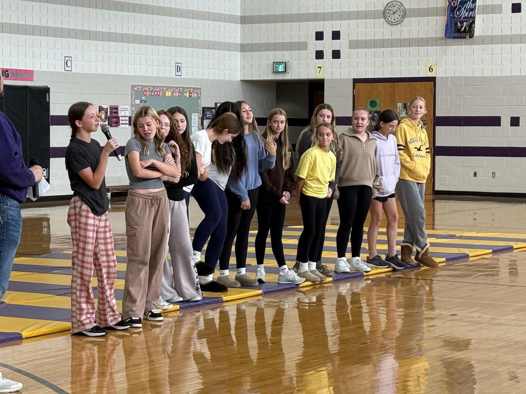 A student with a microphone standing in front of a group of students in the gym.