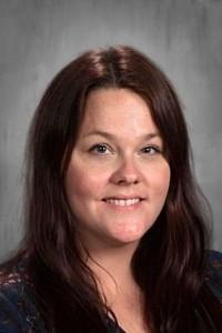 Smiling woman with long brown hair wearing a black patterned blouse.