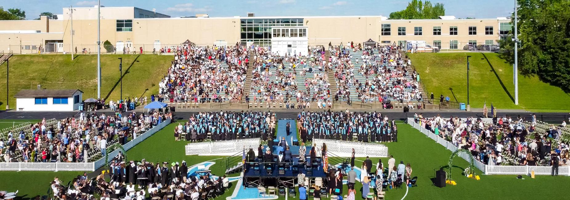 An aerial view of the class of 2026 commencement ceremony with high school in background