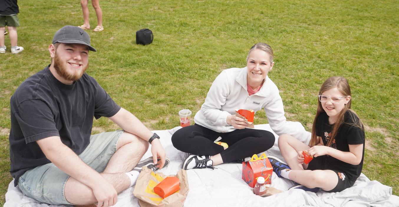 Group of three people sitting on a blanket with fast food outdoors.
