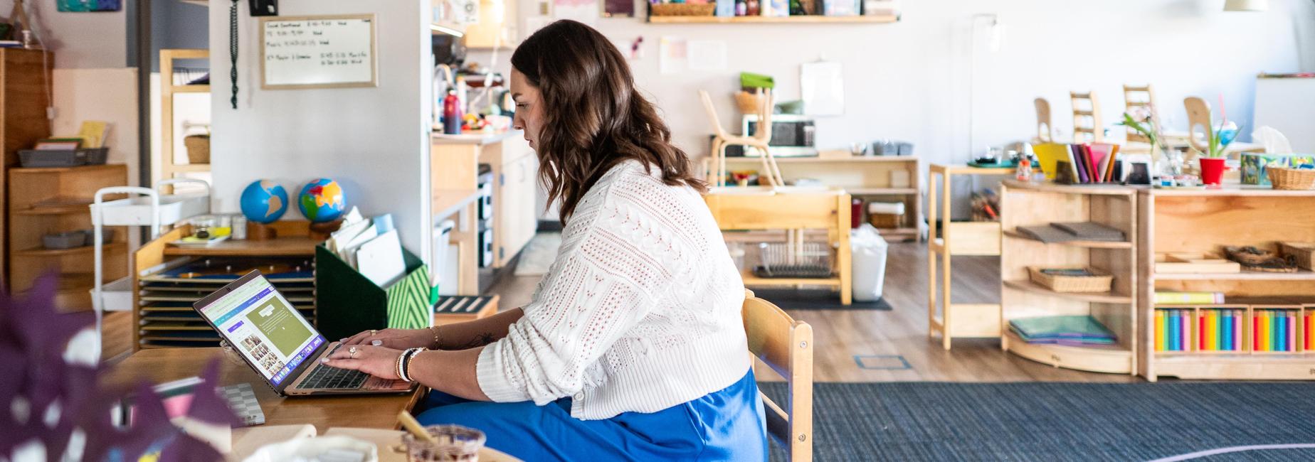 A woman typing on a laptop in a colorful classroom environment.