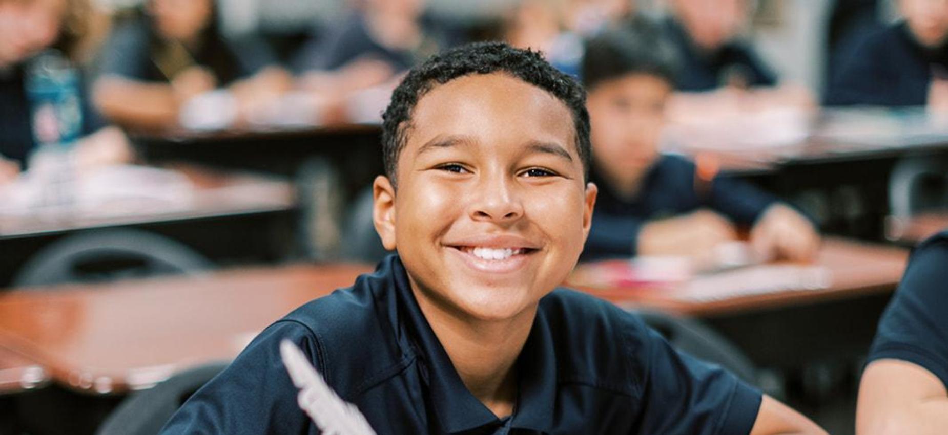 Smiling elementary student writes at his desk