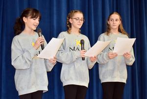 Three girls in grey sweatshirts speaking into microphones