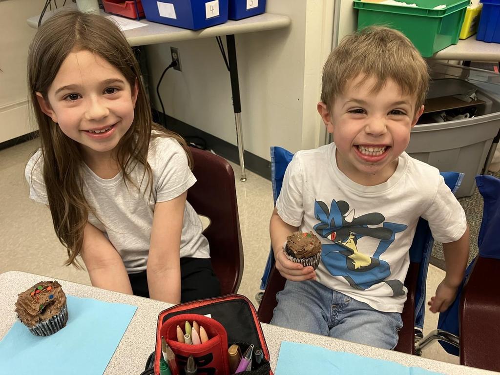 Two students smiling and eating cupcakes.