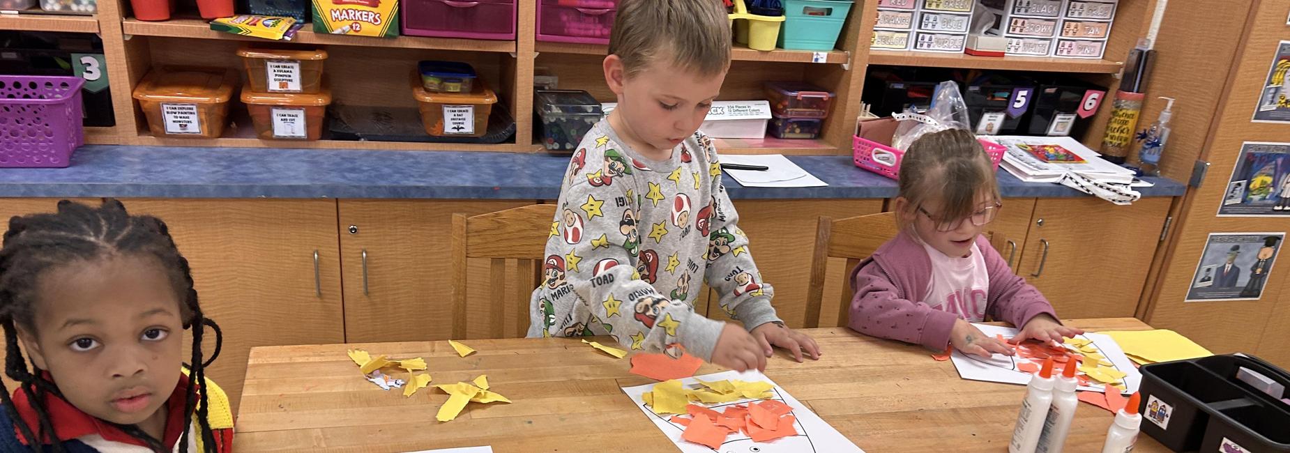 3 students making ripped paper candy corn art.