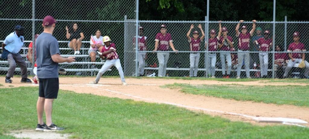 Baseball player at bat with teammates in dugout in the background.