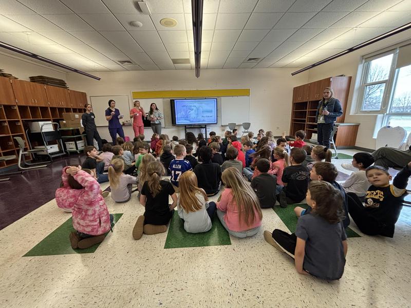 students seated on floor with hygienist in front of room