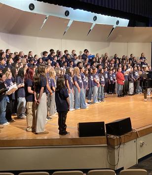 A large group of students performing on stage with a piano