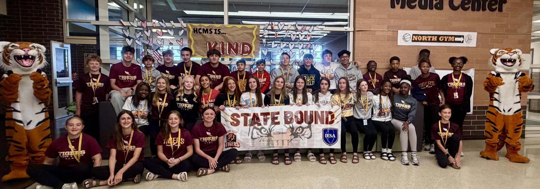 Group of students posing together with a banner in a school setting.