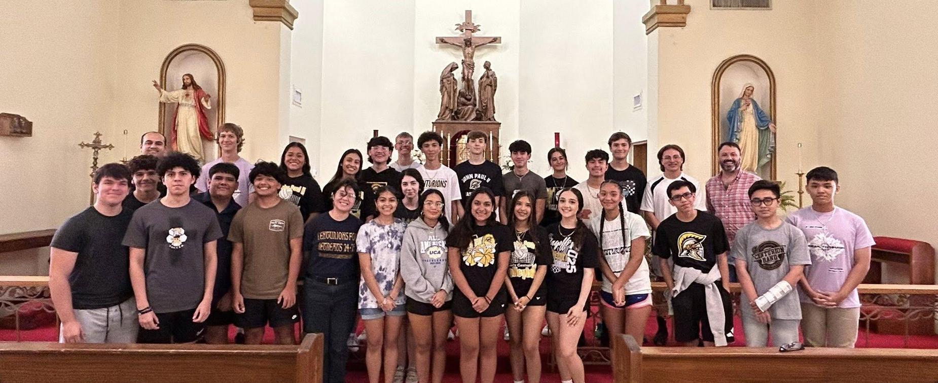 Group of people posing together inside a church with religious statues in the background.