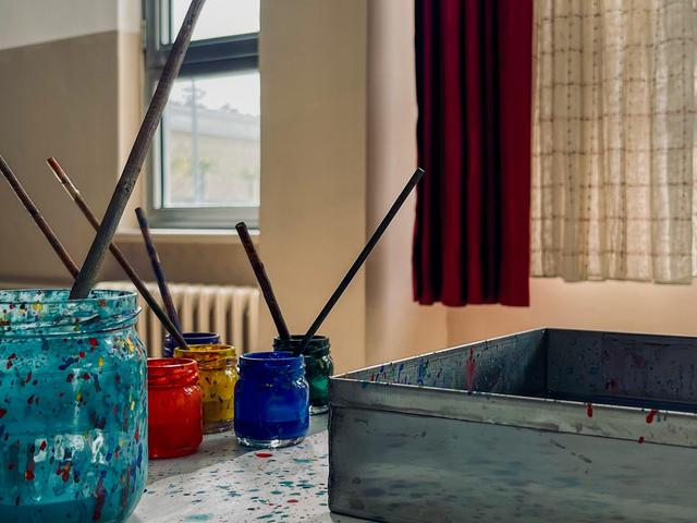 Colorful paint jars and brushes on a table near a window.