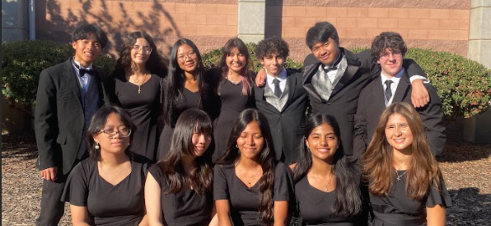 Group of young adults in formal attire posing outdoors in front of a building.