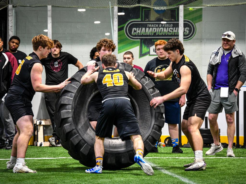High school athletes pushing a large tire in an indoor competition.