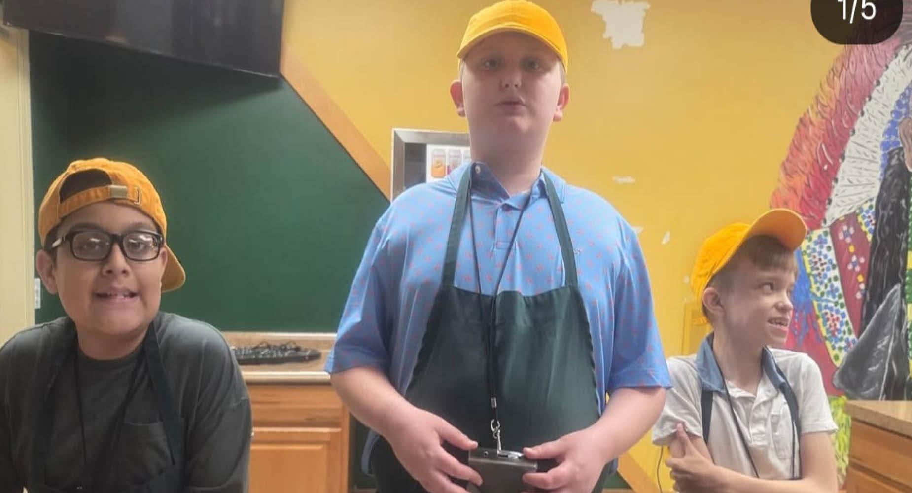 Three children in yellow caps pose for a picture in a kitchen setting.