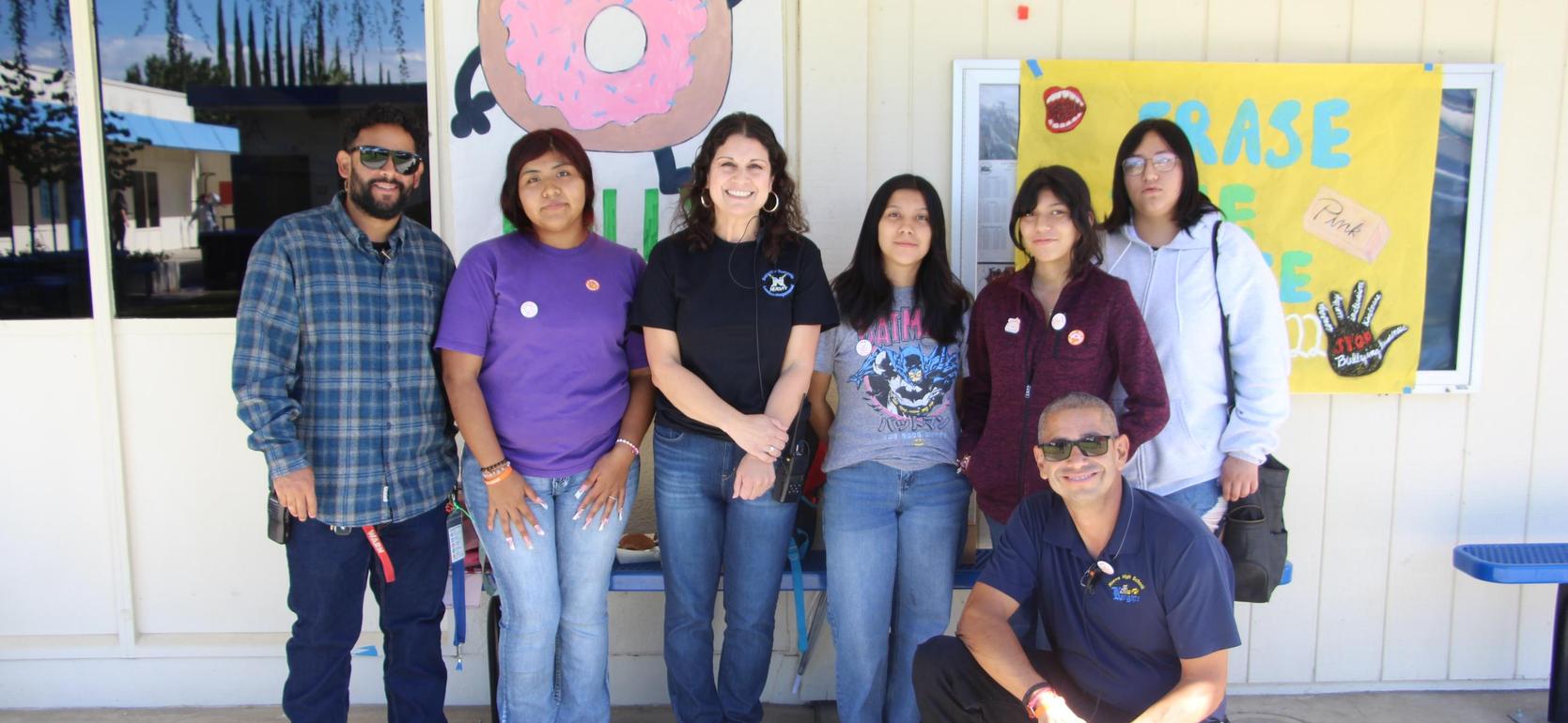 Group of seven people posing in front of a school wall with colorful decorations.