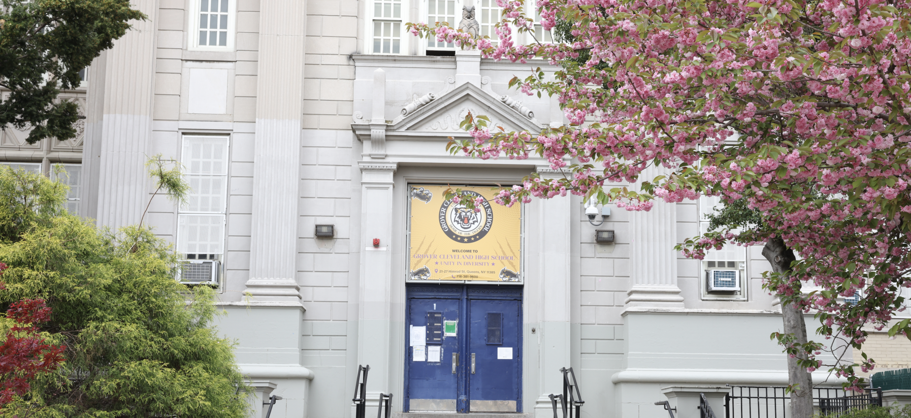School entrance with blue doors framed by blooming trees and decorative architecture.