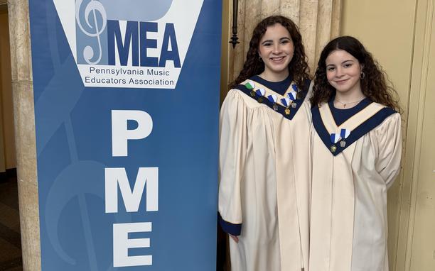 Two students standing next to a PMEA banner.