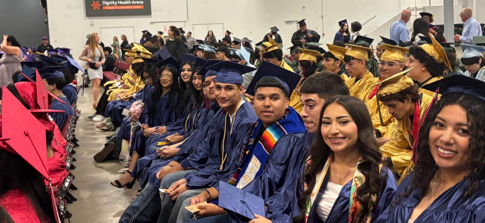 Graduating students in caps and gowns seated in an arena during a ceremony.