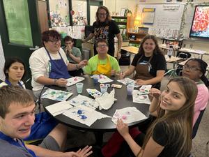 Eight students painting together at a round table in a classroom.