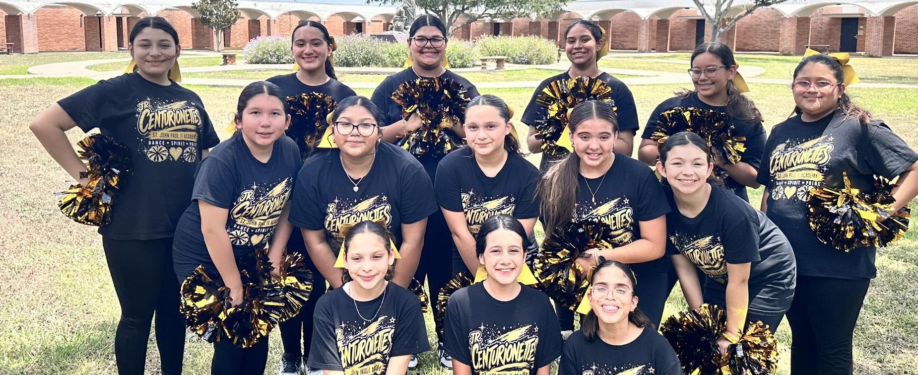 Cheerleading squad posing together outdoors with pom-poms.