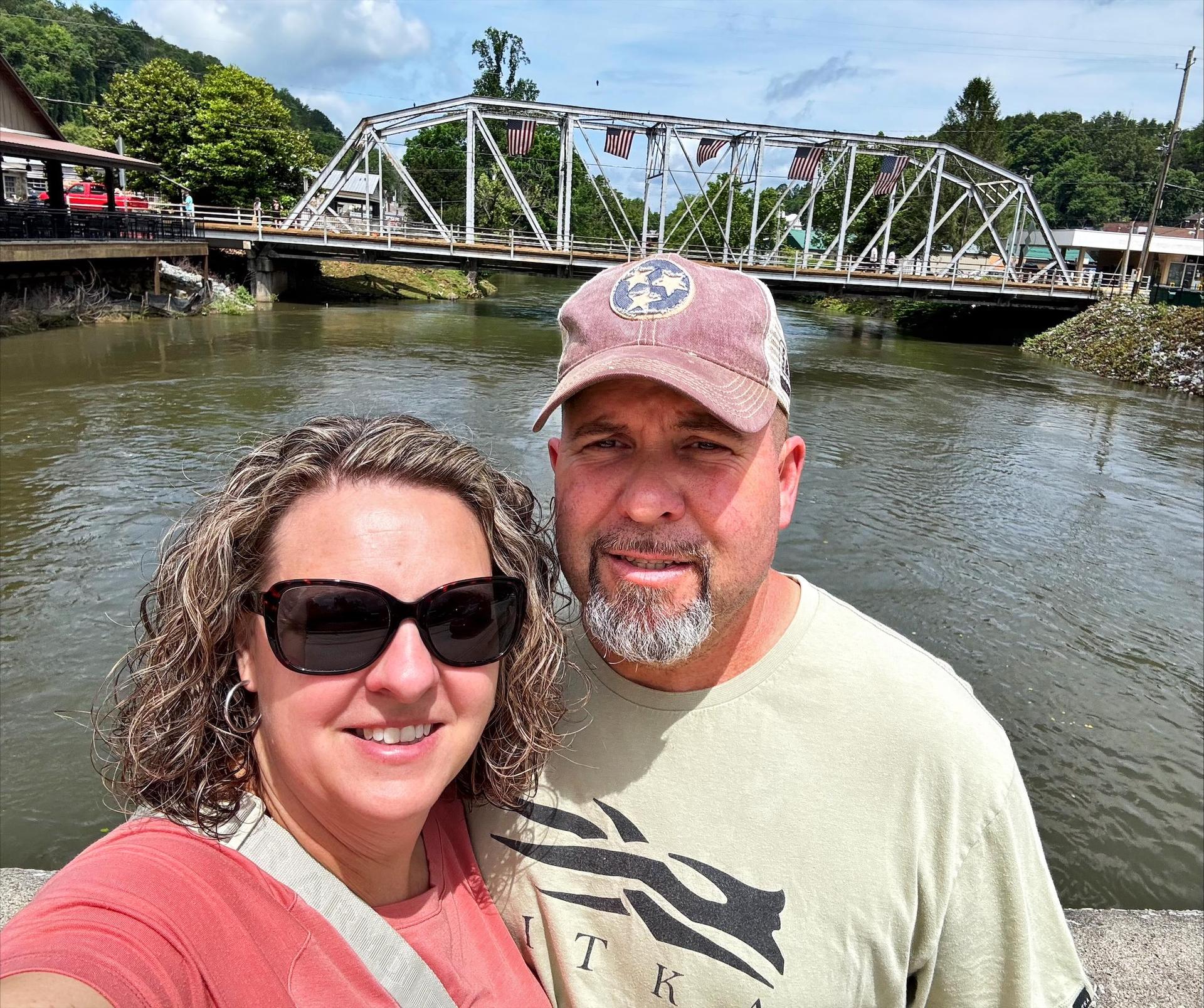 Man and woman in front of water and a bridge.