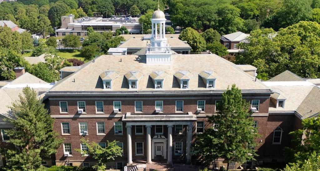 Historic brick building surrounded by trees and manicured lawns.