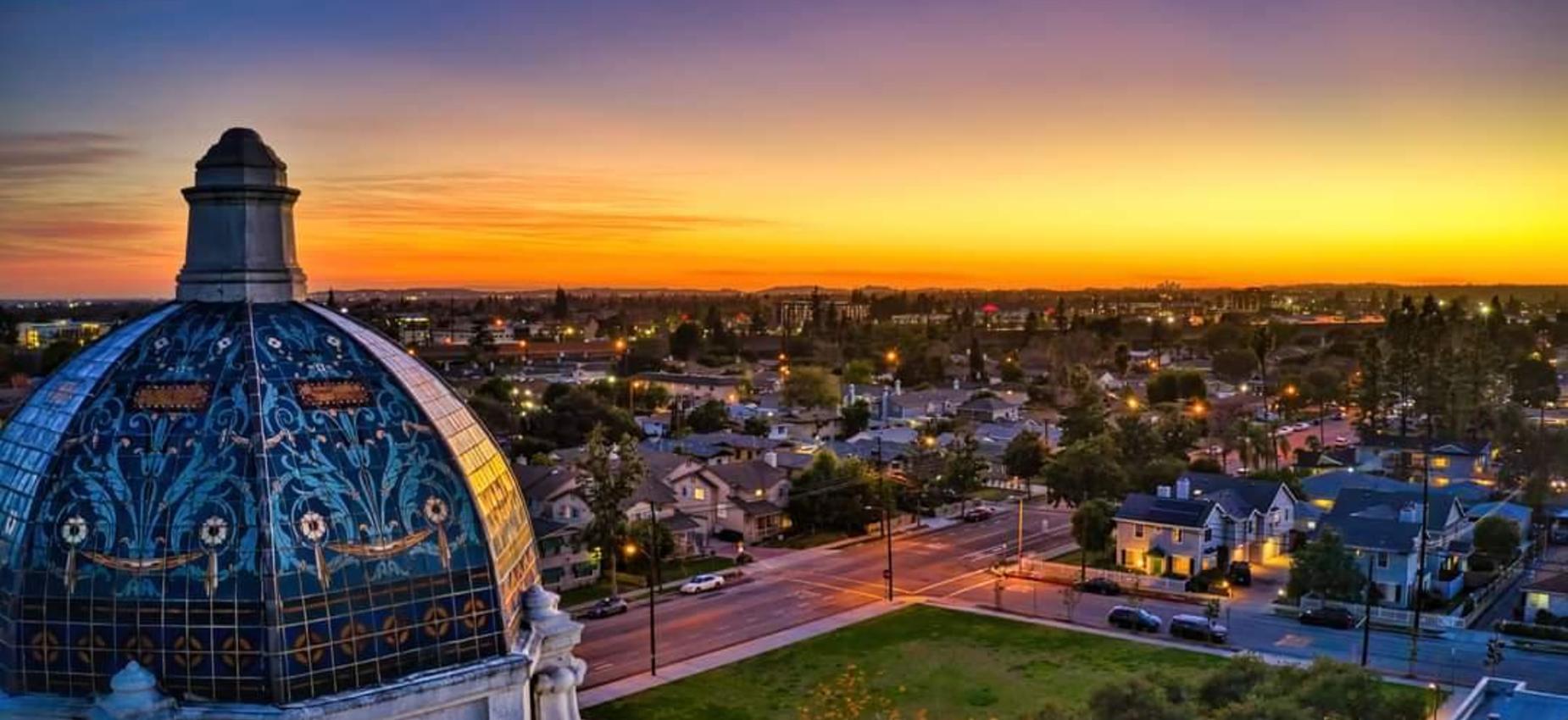 Panoramic view of a city skyline at sunset, featuring a dome in the foreground.