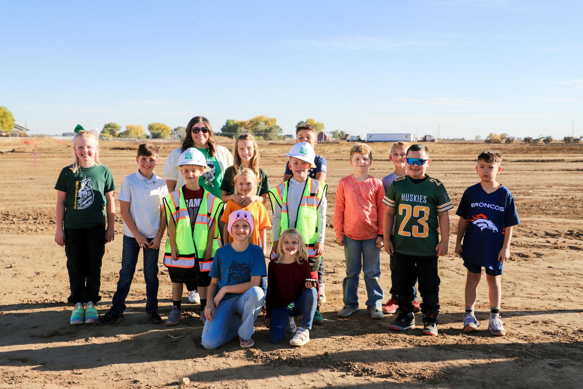 Children and adults in safety vests smiling at a construction site.