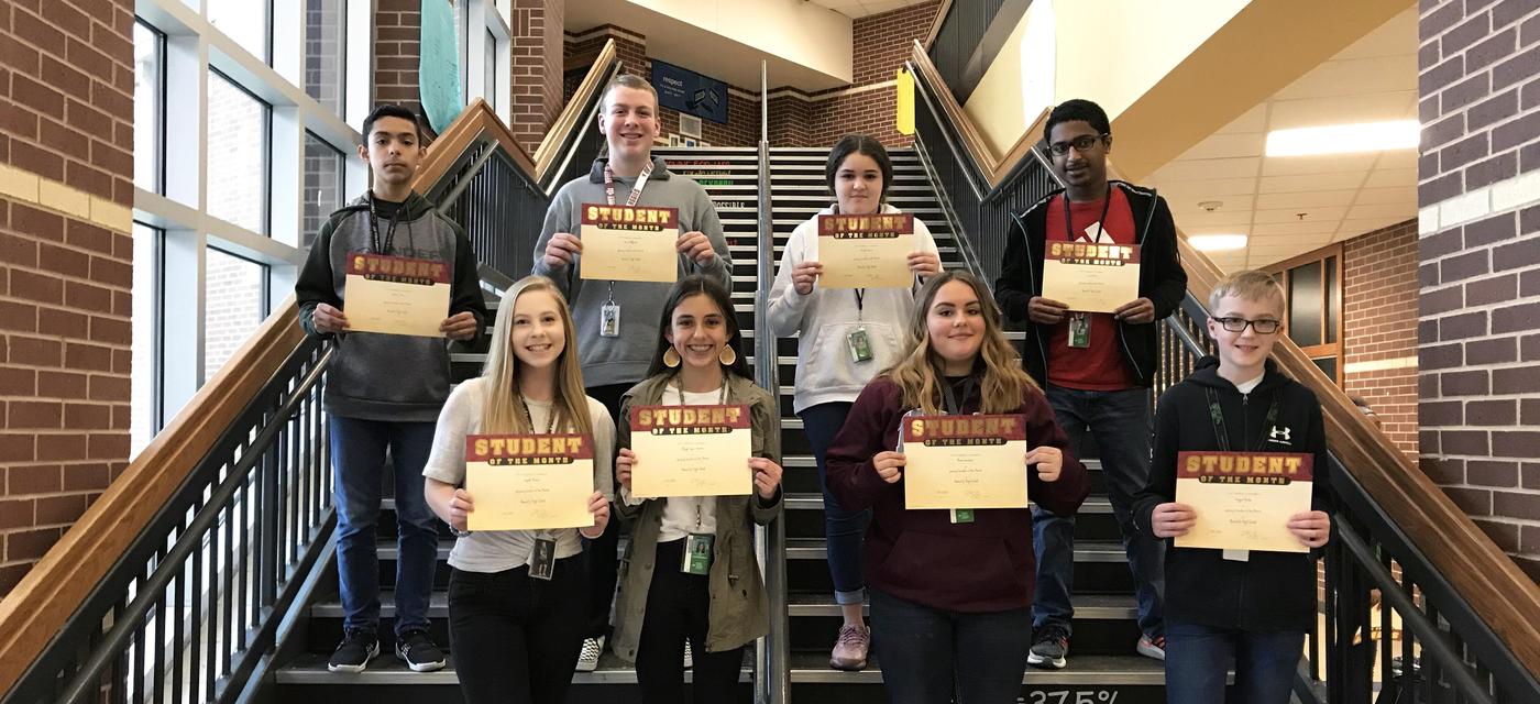 group of 8 students pose on steps with student of the month certificates