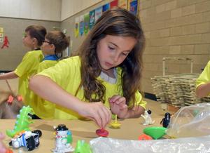 A girl in a yellow shirt focuses on spinning a toy at a table with various small figures.