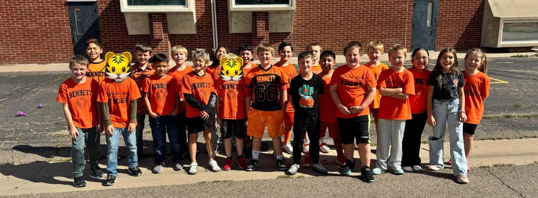 Group of children in orange shirts posing together outside a building.