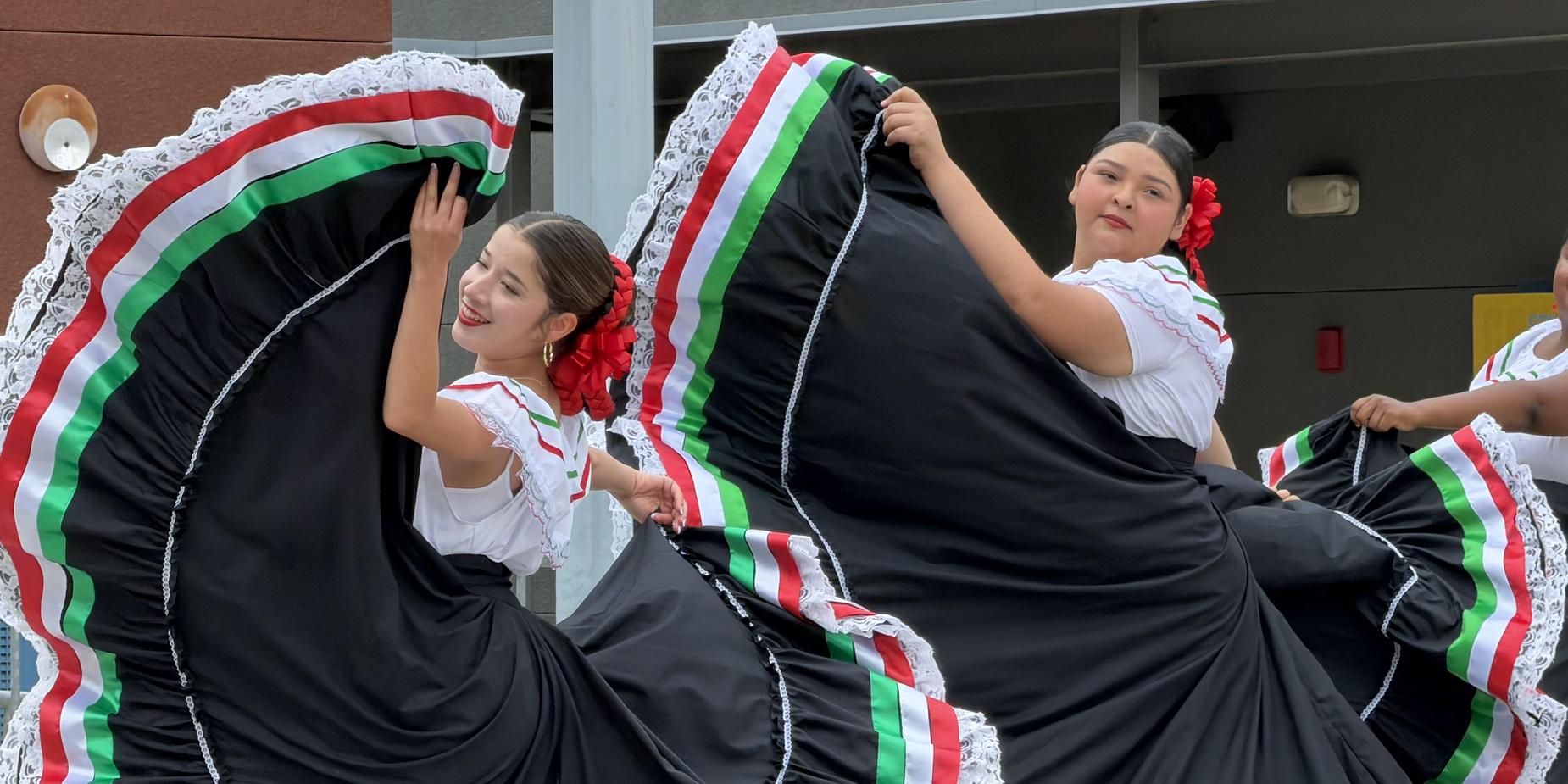 Dancers in colorful traditional dresses perform with flowing skirts.