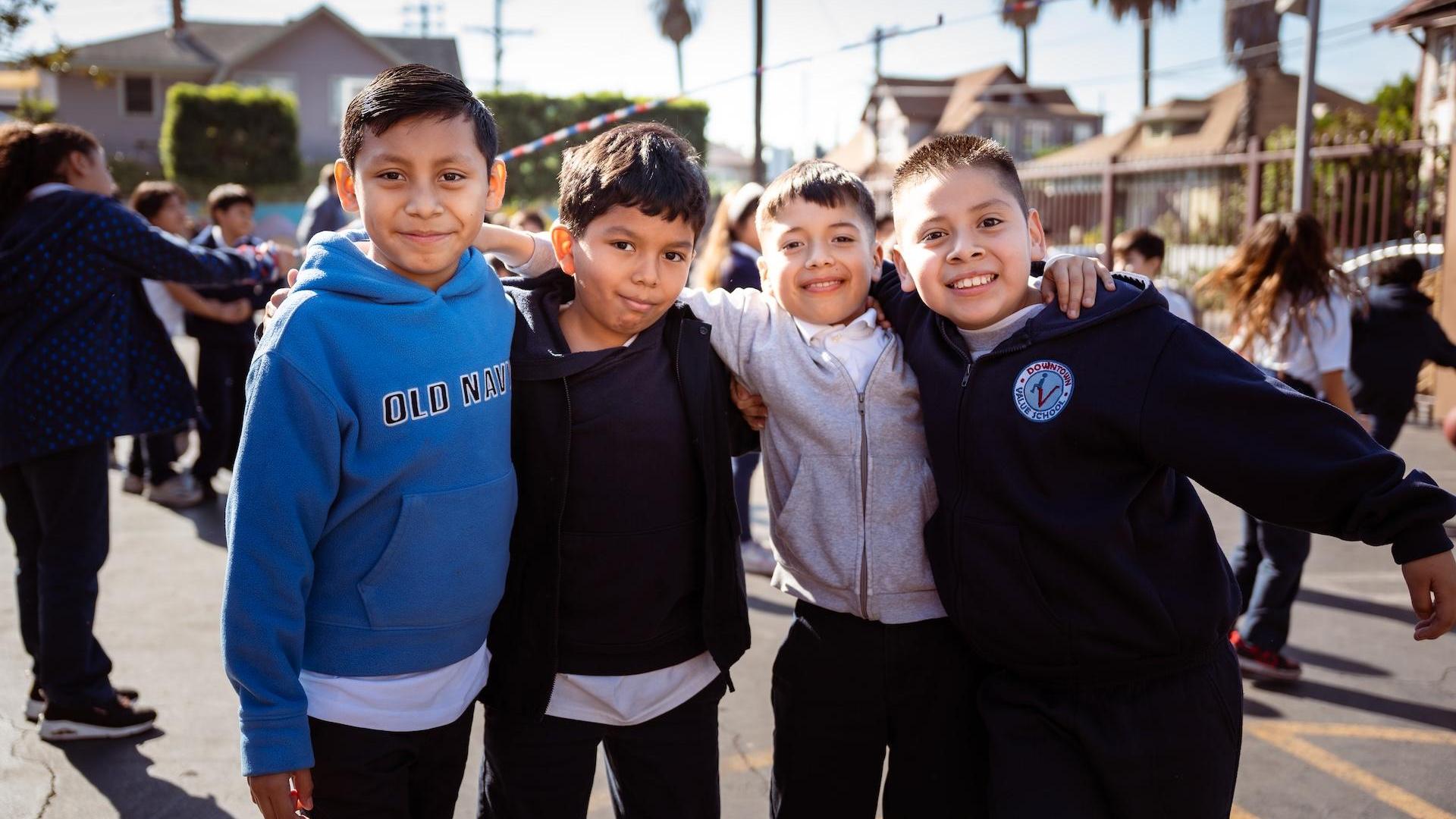 Four smiling boys posing together outdoors in school attire.