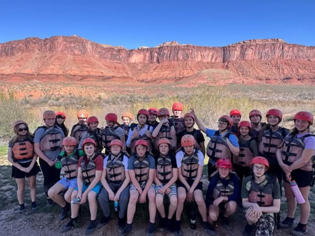Students with hardhats sitting in front of a red mountain range.