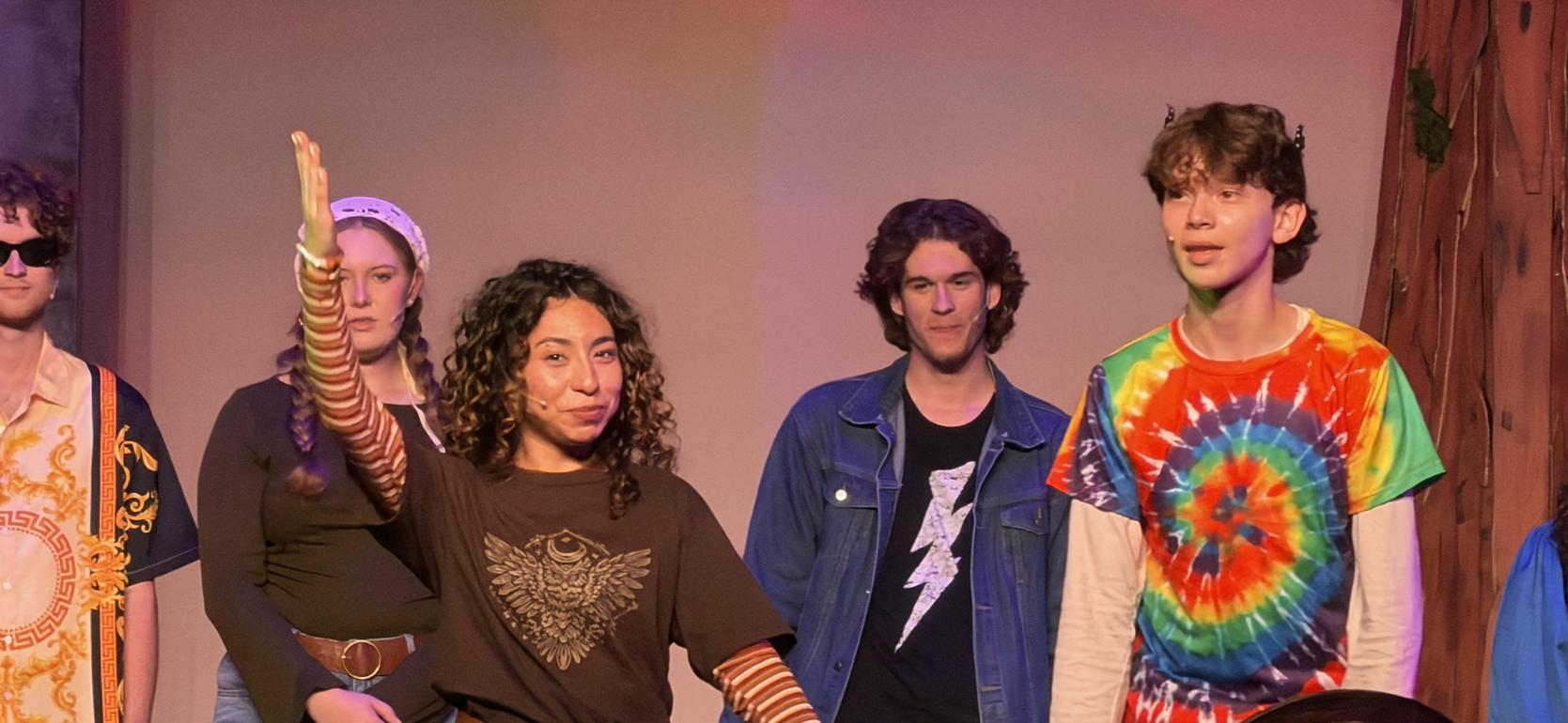 A group of young actors performing on stage, showcasing various costumes and expressions.