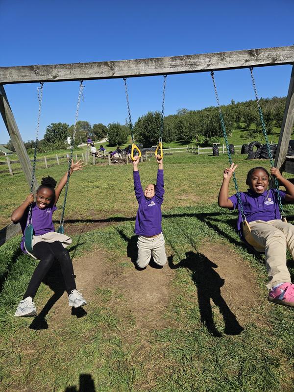 Three scholars on swings outside at the apple orchard