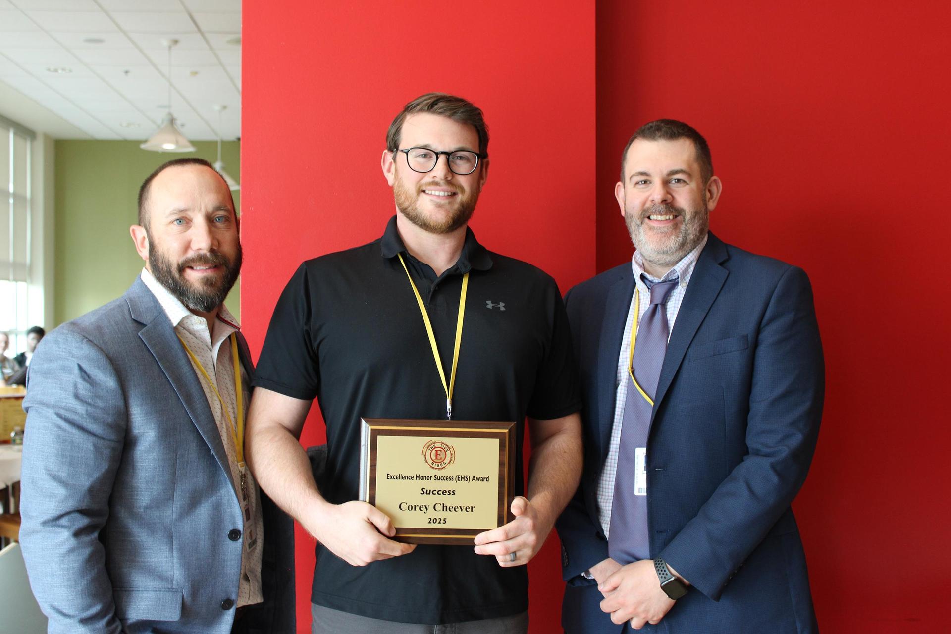 A teacher, standing in between two colleagues, holding an award certificate