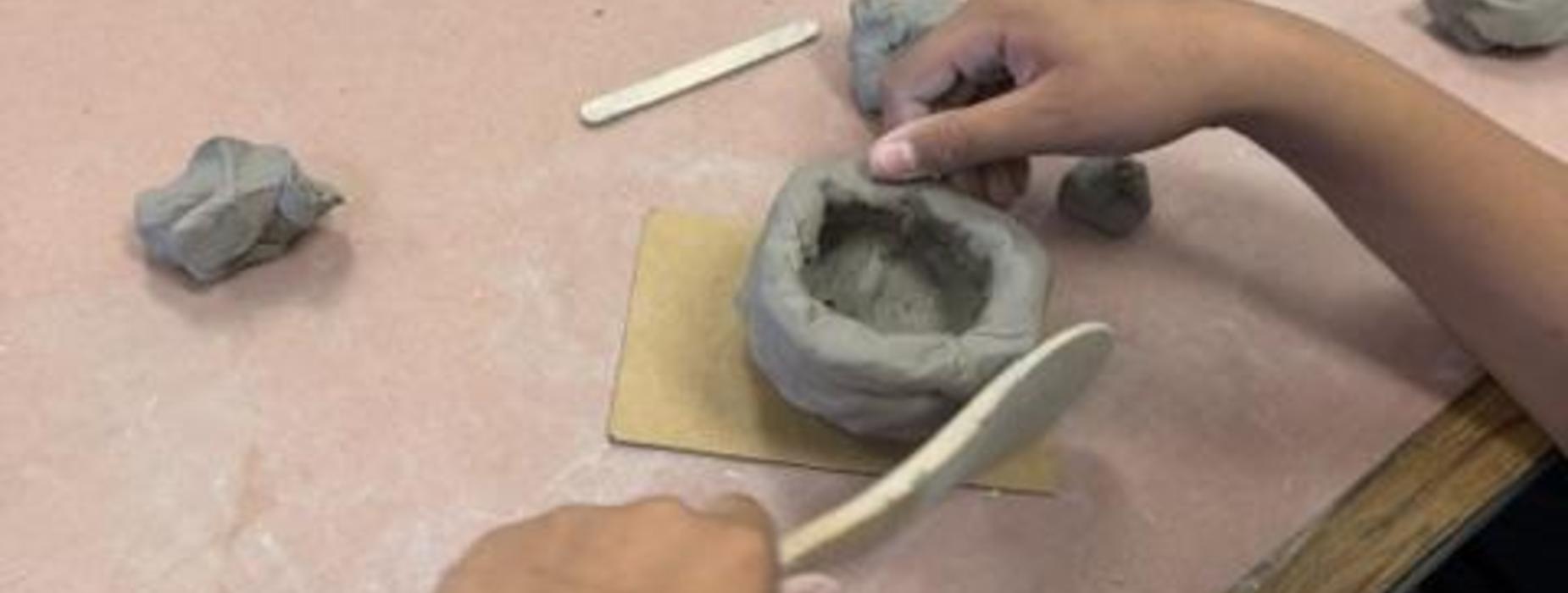 A child's hands shaping clay on a work surface.