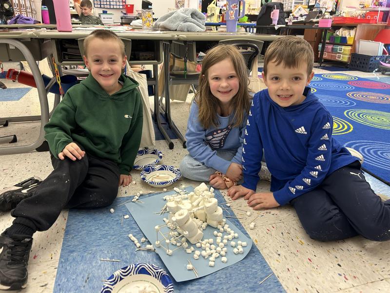 two boys and a girl sitting on floor with a mat full of marshmallows