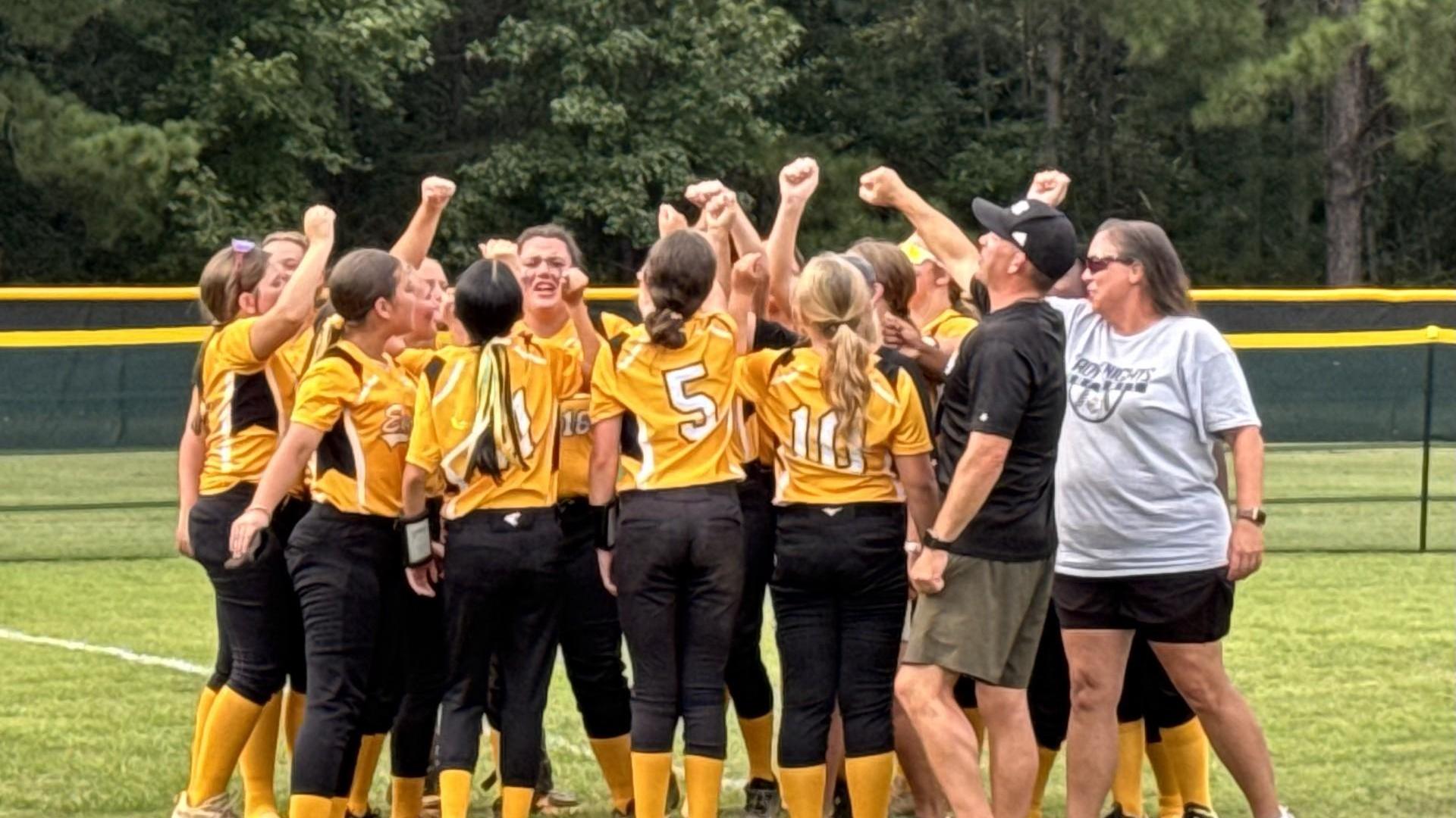 A group of young softball players celebrating with raised fists in team uniforms.