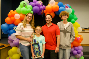 A mom, dad, young boy and older boy hold a trophy together.