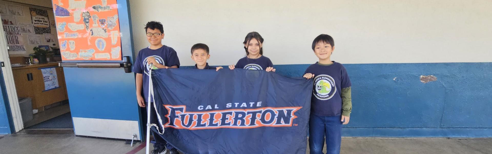 Four children holding a Cal State Fullerton flag in a school hallway.
