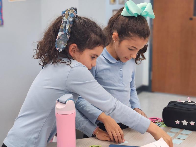 Two girls work together to form a hebrew word using prompt cards.