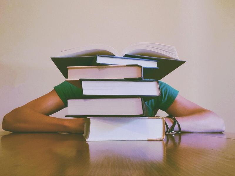 Student resting on a stack of books with an open book on top.