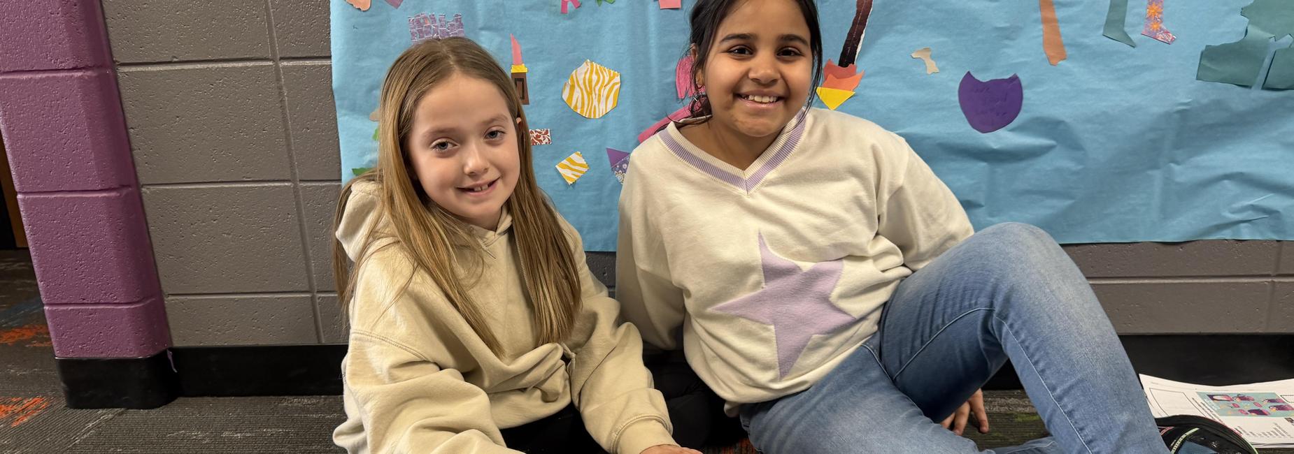 Two children sitting on the floor, one drawing and the other smiling.