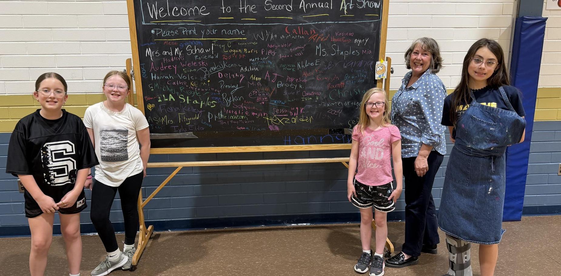 Group of children and adults near a chalkboard at an art show event.