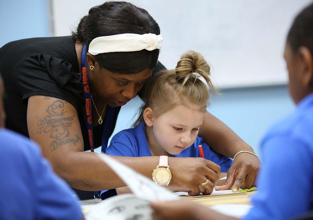 HSA Teacher smiles while working with a young student in a classroom setting.