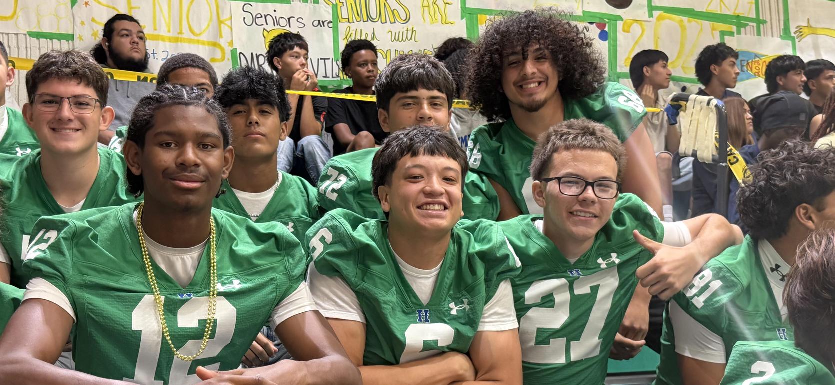 A group of smiling football players in green jerseys posing together.