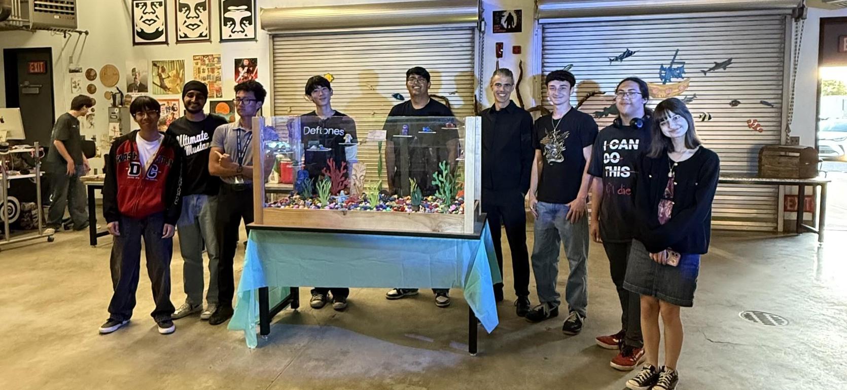 A group of people standing by a decorative aquarium in a workshop space.